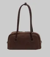 Cartera de mano tipo bowling, confeccionada en gamuza color marrón, con costuras a la vista y manijas largas de cuero al tono.