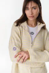 Campera de punto a rayas horizontales en tonos amarillo pastel y lila, con cuello alto, cierre frontal completo y mangas largas con bordado distintivo en la manga.