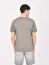 Remera de manga corta color gris jaspeado con cuello redondo. Estampado frontal con diseño de paisaje dividido en dos secciones: una con palmeras y otra con montañas nevadas, con texto que incluye "Expedition", "Summer Times", "Chill Out" y "Chasing The Sun".