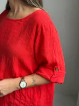 Blusa roja de lino, con cuello redondo, mangas 3/4 con presilla y botones, y diseño holgado con pliegues frontales.