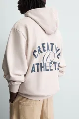 Sudadera hoodie relaxed fit de color beige, con cuello con capucha, manga larga y bolsillo frontal tipo canguro. Presenta un pequeño estampado de texto en contraste en el pecho.
