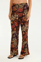 Pantalón acampanado con estampado floral multicolor sobre fondo negro. Corte ajustado con bajo ancho.