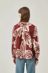 Camisa de poliéster con estampado floral en tonos bordó y crema, de corte holgado, cuello mao y cierre frontal con botones.