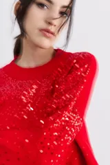 Sweater rojo de tejido de punto con cuello redondo y mangas largas. Diseño con lentejuelas rojas bordadas en el frente y las mangas.