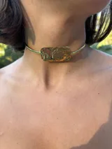 Gargantilla rígida dorada con dije rectangular texturizado.