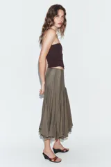 Falda midi de tiro medio confeccionada en tejido fluido con acabado satinado. Presenta diseño con godets que aportan volumen y movimiento, y bajo con detalle de encaje a tono. Cierre lateral con cremallera oculta.