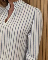 Blusa blanca de algodón con escote en V y cuello mao. Presenta mangas largas abullonadas con puños acampanados y fruncidos.