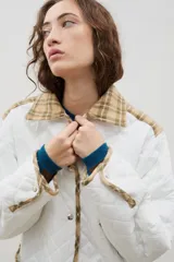 Campera acolchada de corte holgado, color blanco con diseño capitoneado en forma de rombos. Presenta cuello camisero y bordes internos con estampado floral en tonos azul y rojo, cierre frontal con botones a presión y bolsillos laterales.