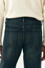 Jean de cinco bolsillos en denim de algodón rígido, color azul oscuro lavado. Modelo de cintura clásica con cierre de botón y corte relajado de cadera a bajo con pierna recta más amplia a partir del muslo.