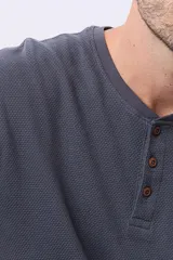 Remera de algodón texturada color gris oscuro, de manga larga, con cuello redondo y botones en la parte frontal. Presenta un pequeño logo bordado en el pecho y un parche decorativo en la manga izquierda.