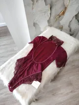 Body de lycra color bordó con cuello alto, mangas cortas y espalda descubierta. Presenta detalles de encaje en el cuello, mangas y laterales de la parte inferior. Cuenta con cierre de broches en la entrepierna.