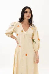 Vestido largo blanco de algodón con bordados de motivos marinos en tonos naranja, verde y azul. Tiene escote en V, mangas 3/4 abullonadas y cierre frontal con botones.