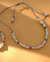 Collar artesanal compuesto por piezas metálicas irregulares con acabado dorado, ensartadas en un cordón de hilo de algodón natural. Presenta un sistema de nudo corredizo para ajustar el largo.