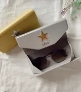 Estuche para lentes plegable con diseño rígido y cierre magnético. Presenta una estrella metálica decorativa en la solapa frontal y el logo de la marca estampado. El interior está forrado en material suave para proteger los cristales.