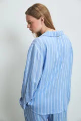 Pijama de dos piezas confeccionado en viscosa, compuesto por una camisa de manga larga con cuello solapa y cierre frontal de botones, y un pantalón de corte recto y holgado. Presenta un diseño de rayas verticales en tonos azul y blanco.