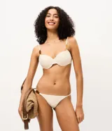 Bombacha de bikini colaless color beige, confeccionada en microfibra acanalada con laterales finos y detalle de aplique circular carey en el lateral derecho.