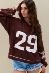 Sweater de punto marrón chocolate, con diseño oversize, cuello en V, mangas largas con estrellas blancas estampadas y número grande en el frente.