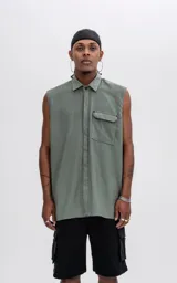 Camisa sin mangas color verde militar, con cuello, cierre frontal de botones y un bolsillo de parche con tapa en el pecho izquierdo. Presenta un calce oversize.