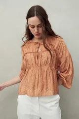 Blusa estampada de caída fluida con cuello redondo y lazos frontales, diseño con cortes horizontales y frunces, mangas largas con puños elastizados.