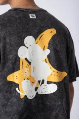 Remera de algodón con efecto acid wash en color gris oscuro. Presenta un diseño estampado en el pecho con una estrella amarilla y un personaje animado, y un corte semi-oversize.