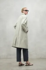 Chaqueta tipo trench color beige, de corte holgado y largo midi. Presenta cuello camisero, cierre frontal con botones a tono y mangas largas. Confeccionada en tejido repelente al agua.