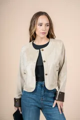 Chaqueta corta color beige, con cuello redondo, cierre frontal con botones dorados, bolsillos de parche y puños en contraste color marrón.