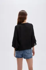 Blusa negra de poliéster, con cuello redondo, mangas 3/4 con volados en capas y diseño holgado.