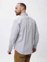 Camisa de manga larga con estampado de microcuadros en tonos azul y blanco. Presenta cuello clásico con botones, cierre frontal abotonado y detalle de logo bordado en el pecho.