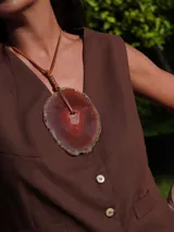 Collar con dije de piedra ágata blanca y marrón, con forma circular irregular y agujero en el centro. El dije está sujeto con un cordón fino de cuero marrón.