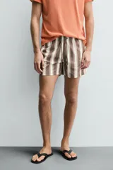 Bañador de hombre con estampado de rayas verticales anchas en tonos marrón oscuro y beige claro, con finas líneas rosadas entre ellas. Posee cintura elástica con cordón ajustable y forro interior.