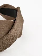 Vincha de diseño trenzado en color marrón con acabado satinado y estructura interna de plástico negro.