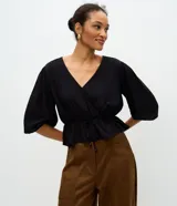 Blusa peplum de viscosa negra con escote en V cruzado, mangas cortas abullonadas con elástico en los puños y cordón ajustable en la cintura.