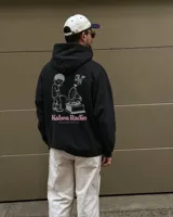 Canguro negro con capucha, de corte regular y confección en felpa suave, con estampa en la espalda de un personaje gráfico y texto "Kaboa Radio".