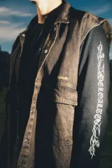 Chaleco de denim negro con efecto deslavado, diseño sin mangas, bolsillos frontales con solapa, costuras en contraste y botones metálicos.