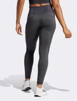Calza deportiva Adidas Seamless 7/8 de tiro alto, color negro, confeccionada con tejido suave y elástico sin costuras con tecnología AEROREADY. Presenta diseño de líneas acanaladas en la cintura y los tobillos, y las tres tiras características de la marca en el muslo derecho.
