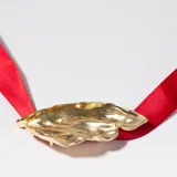Colgante con dije dorado con forma orgánica irregular y cinta de raso roja.
