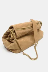 Bolso de hombro de piel color tostado con diseño acolchado y costuras geométricas. Cuenta con tres compartimentos, uno de ellos con cierre de cremallera, y solapa con cierre magnético. Incluye asa combinada de piel y cadena metálica dorada.