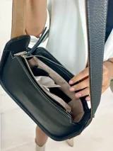 Bolso baguette de cuero negro con asa reversible y logo de la marca en etiqueta de cuero marrón.