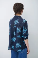 Camisa de corte clásico con cuello camisero y cierre frontal de botones, confeccionada en tela color bordó con estampado floral en tonos celestes.