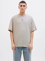 Remera beige de manga corta y cuello redondo con estampado en la espalda con la inscripción "Atelier © 1990" y un diseño abstracto en tonos lila y naranja.