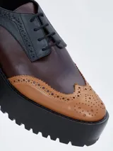 Zapato estilo brogue con plataforma y taco ancho, confeccionado en cuero bicolor con detalles perforados en la puntera y los laterales.