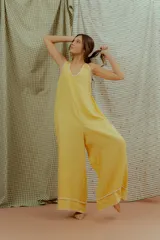 Mono largo de lino color amarillo, con escote en V, tirantes finos y detalles de costuras decorativas blancas en el escote y en los bajos de las piernas anchas.