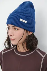 Gorro de lana azul de punto acanalado con vuelta y pequeña etiqueta blanca frontal con la inscripción 'Autumn.'.