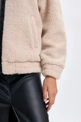 Campera de sherpa color crudo con detalles en cuero sintético negro en el cuello y la solapa frontal. Cuenta con cierre frontal y cuello alto con hebilla ajustable.