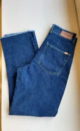 Pantalón de jean azul oscuro, de corte recto y tiro medio, con detalle de ruedo desflecado.