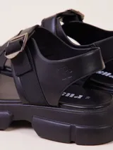 Sandalias negras con plataforma, tiras anchas de cuero sintético y ajuste con hebilla metálica.