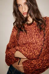 Jersey de punto grueso con textura trenzada en color naranja y bordó. Presenta cuello redondo, mangas largas abullonadas y detalle de cordones trenzados a contraste en el frente con terminación en lazada en el ruedo.