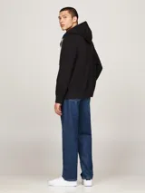 Buzo con capucha y cierre frontal, color negro, confeccionado en felpa de mezcla de algodón. Posee cordón blanco en la capucha, dos bolsillos delanteros tipo canguro y puños y bajo de punto canalé. Lleva un pequeño logo bordado de Tommy Hilfiger en el pecho.