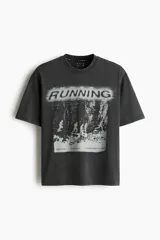 Remera deportiva de corte boxy y holgado con tecnología DryMove, en color gris oscuro con efecto gastado. Presenta hombros caídos, cuello redondo ribeteado y un gran estampado frontal en tonos claros con la palabra 'RUNNING' y siluetas de personas corriendo.