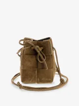 Cartera tipo bucket de cuero gamuzado color marrón, con diseño de paneles entrelazados y cierre mediante lazo ajustable. Incluye correa larga para llevar cruzada.